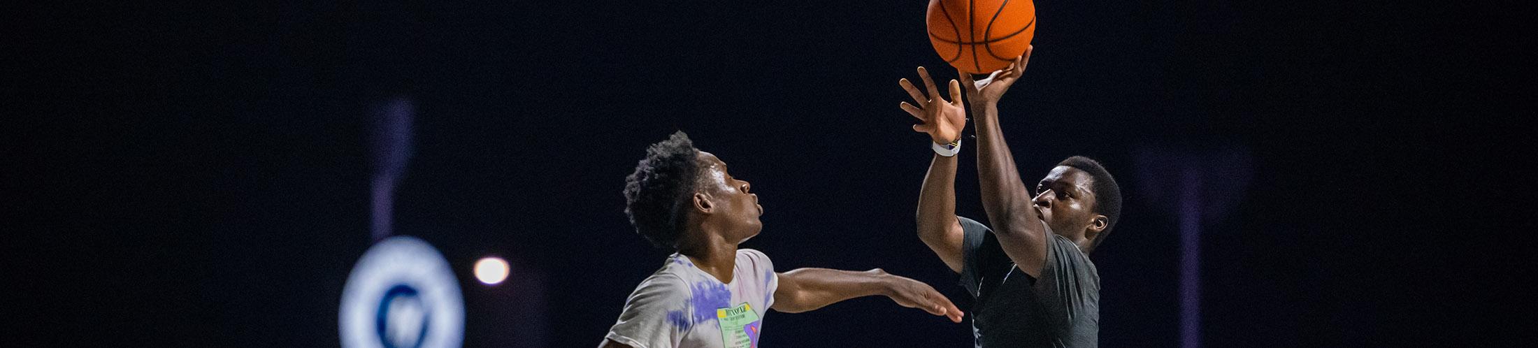 Two students playing basketball with Hancok Whitney in background.